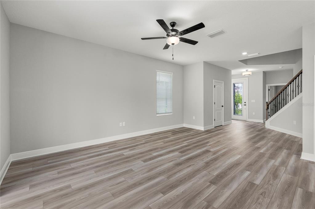 An empty living room features light gray walls, wood-look flooring, a ceiling fan, and stairs — 7737 SOMERSWORTH DRIVE, KISSIMMEE, FL