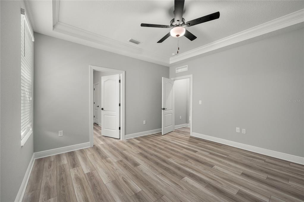 An empty bedroom features light gray walls, wood-look flooring, a ceiling fan, and two doorways — 7737 SOMERSWORTH DRIVE, KISSIMMEE, FL