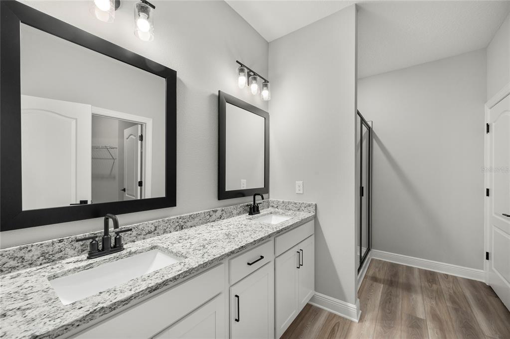 A bathroom features a double vanity with white cabinets, granite countertops, and black framed mirrors — 7737 SOMERSWORTH DRIVE, KISSIMMEE, FL