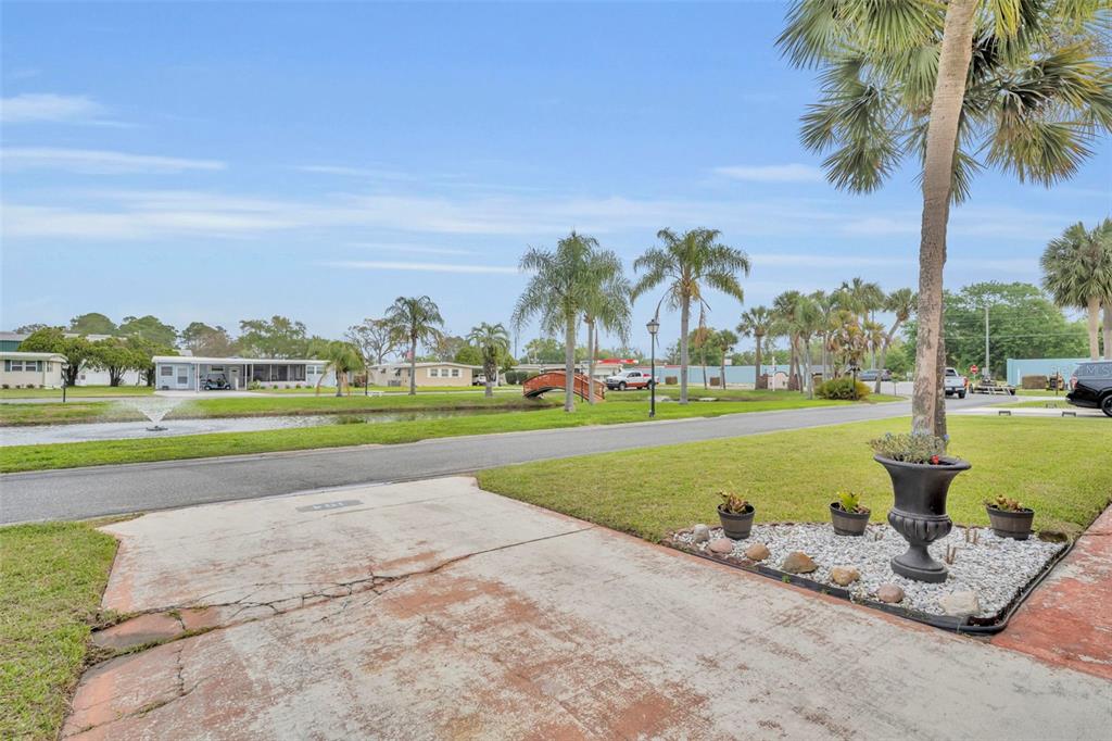 A view from a driveway looking toward a small pond, a wooden bridge, and palm trees — 104 DIAMOND HEAD DRIVE, LEESBURG, FL