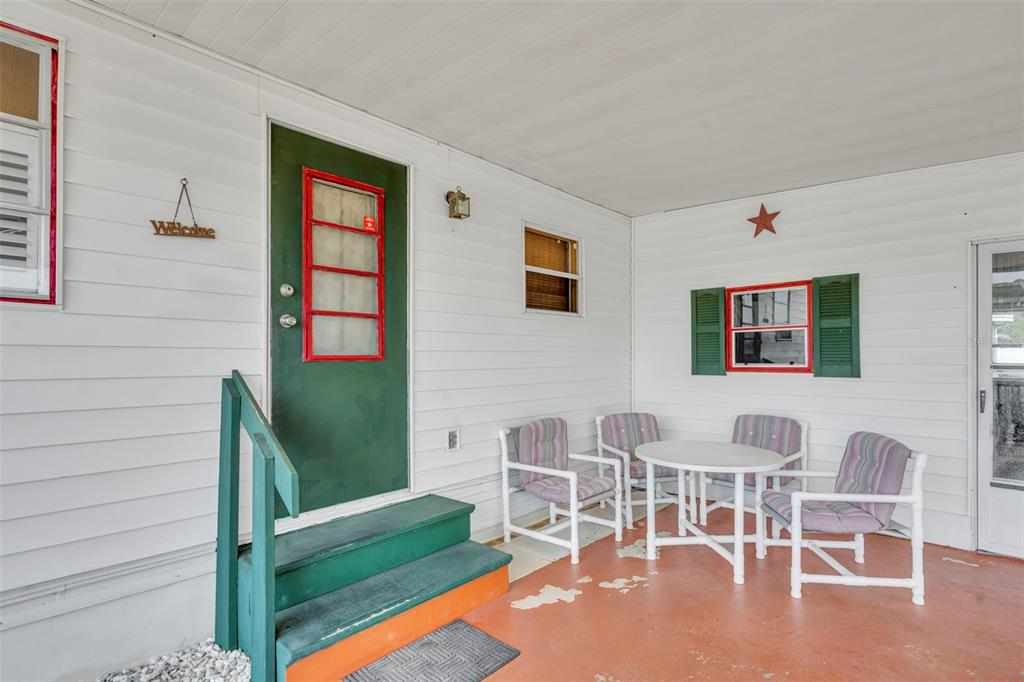 A covered porch features white siding, a green door, and a small outdoor dining set — 104 DIAMOND HEAD DRIVE, LEESBURG, FL