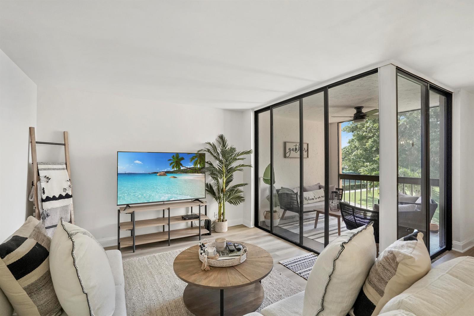 A living room features a television, a round coffee table, and sliding doors to a balcony — 750 Egret Circle # 6304, Delray Beach FL 33444, DELRAY BEACH, FL