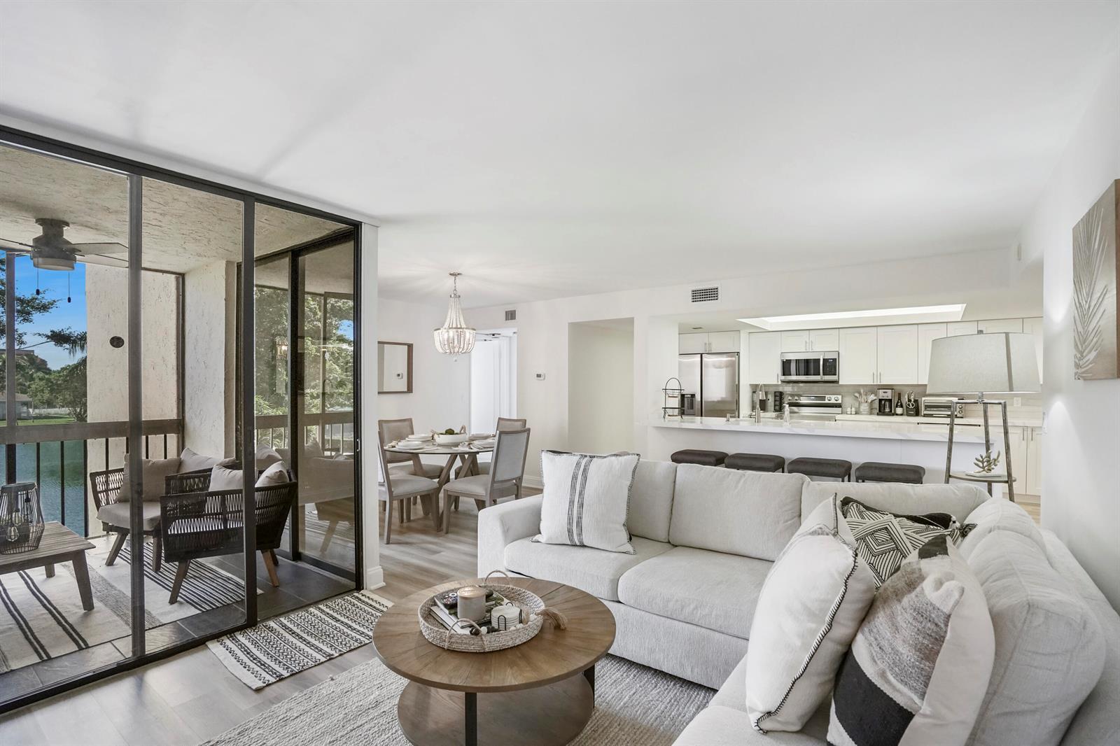 A living room with a white sofa, round coffee table, and adjacent balcony overlooking water — 750 Egret Circle # 6304, Delray Beach FL 33444, DELRAY BEACH, FL