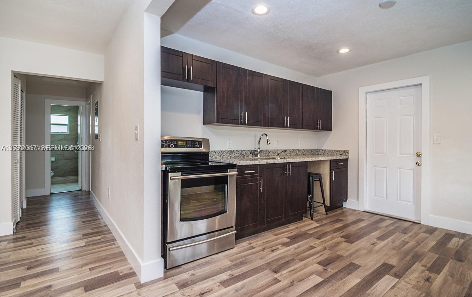 A kitchen features dark wood cabinets, stainless steel appliances, granite countertops, and wood-look flooring — 2542 Fillmore St, Hollywood FL 33020, HOLLYWOOD, FL