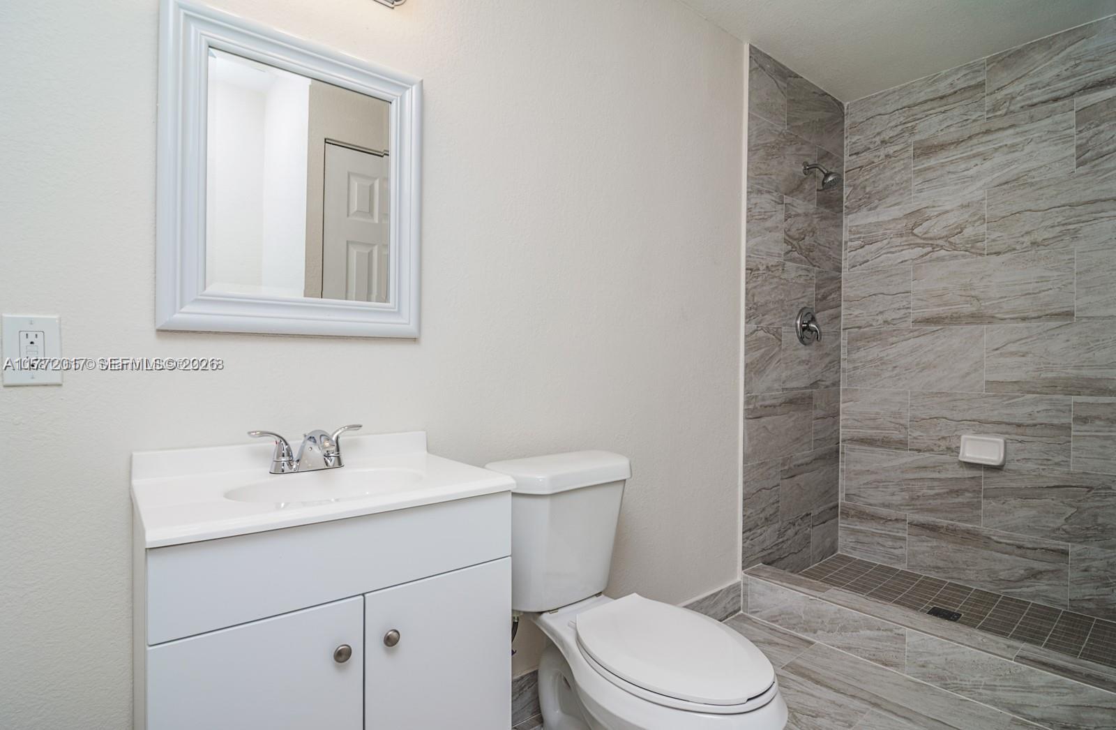 A bathroom features a white vanity, a toilet, and a walk-in shower with tiled walls — 2542 Fillmore St, Hollywood FL 33020, HOLLYWOOD, FL