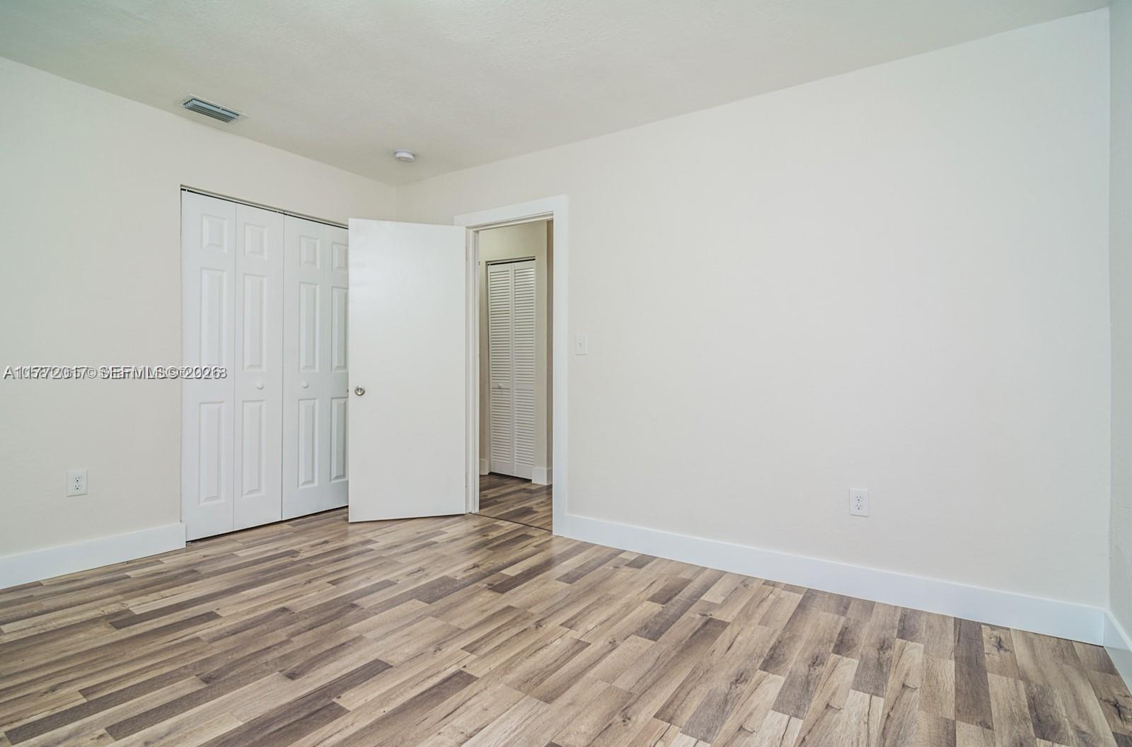 An empty bedroom features white walls, a closet with bi-fold doors, and wood-look flooring — 2542 Fillmore St, Hollywood FL 33020, HOLLYWOOD, FL