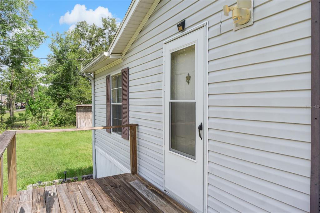 A wooden deck leads to a white storm door on the side of a vinyl-sided house — 4350 S SONGBIRD DRIVE, LECANTO, FL