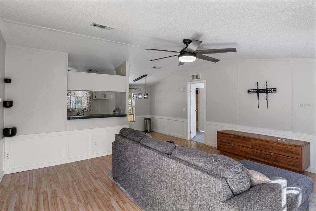 A living room features a gray sofa, wood-look flooring, a ceiling fan, and a pass-through window — 4350 S SONGBIRD DRIVE, LECANTO, FL