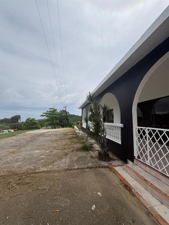 A black exterior wall with arched openings and a white railing overlooks a dirt yard — URB EL MADRIGAL MARGINAL NORTE, PONCE, PR