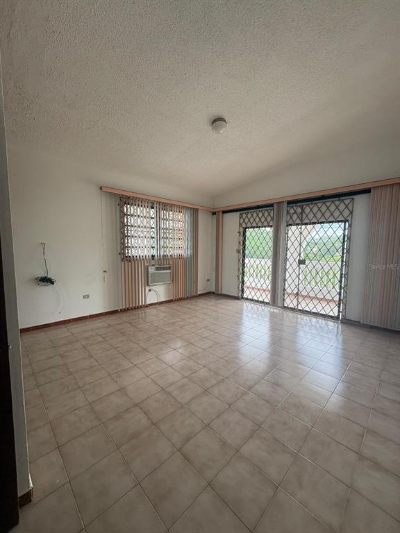 An empty living room features light-colored tile floors, a window air conditioner, and security bars — URB EL MADRIGAL MARGINAL NORTE, PONCE, PR