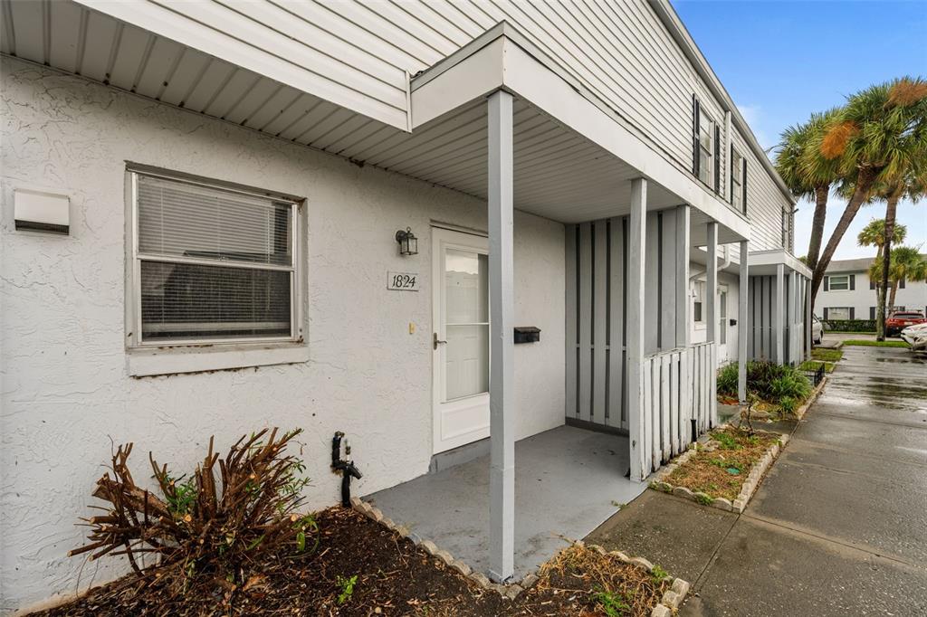 A white stucco townhouse exterior features a covered entryway, a window, and a small garden — 1824 AMBERLY AVENUE UNIT T8, ORLANDO, FL