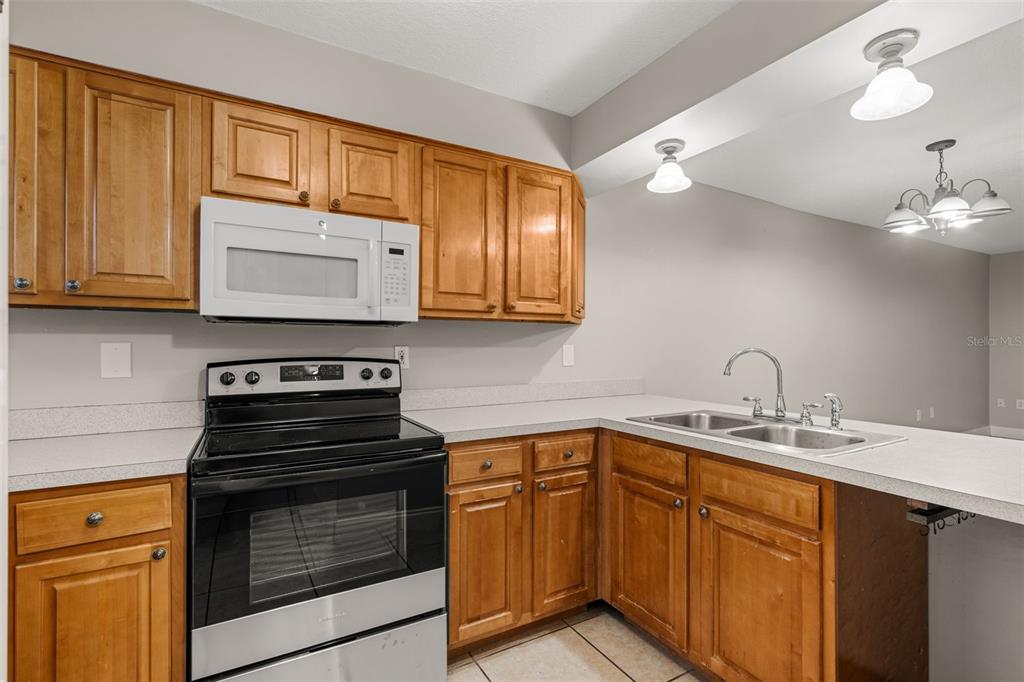 A kitchen with wood cabinets, a black stove, a white microwave, and light countertops — 1824 AMBERLY AVENUE UNIT T8, ORLANDO, FL