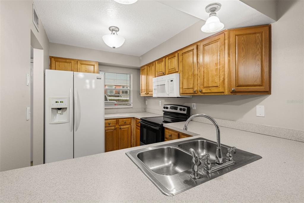 A kitchen features light-colored countertops, wooden cabinets, a white refrigerator, and a double-basin sink — 1824 AMBERLY AVENUE UNIT T8, ORLANDO, FL
