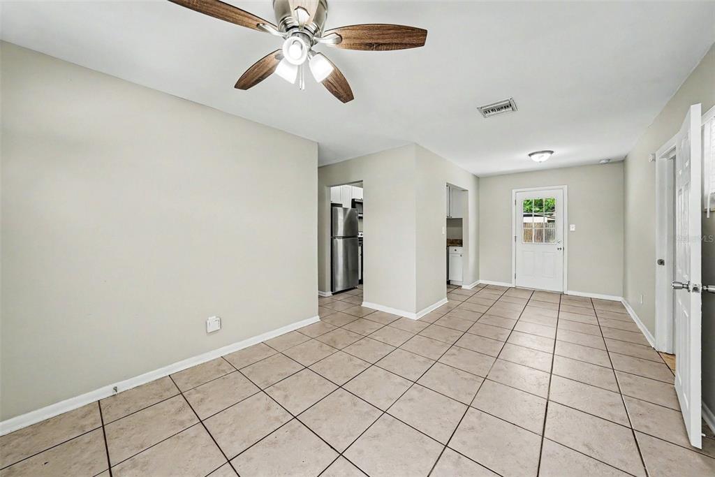 A room with light-colored tile flooring, a ceiling fan, and a doorway leading to a kitchen — 10209 N 28TH STREET, TAMPA, FL