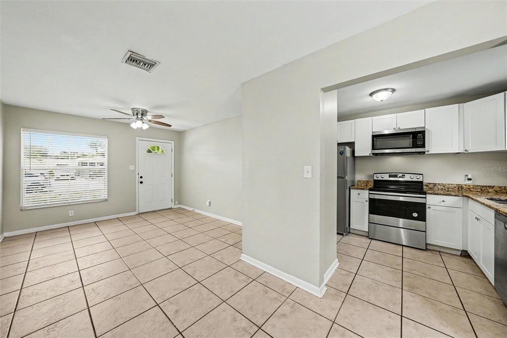A kitchen with white cabinets and stainless steel appliances opens to a tiled dining area — 10209 N 28TH STREET, TAMPA, FL