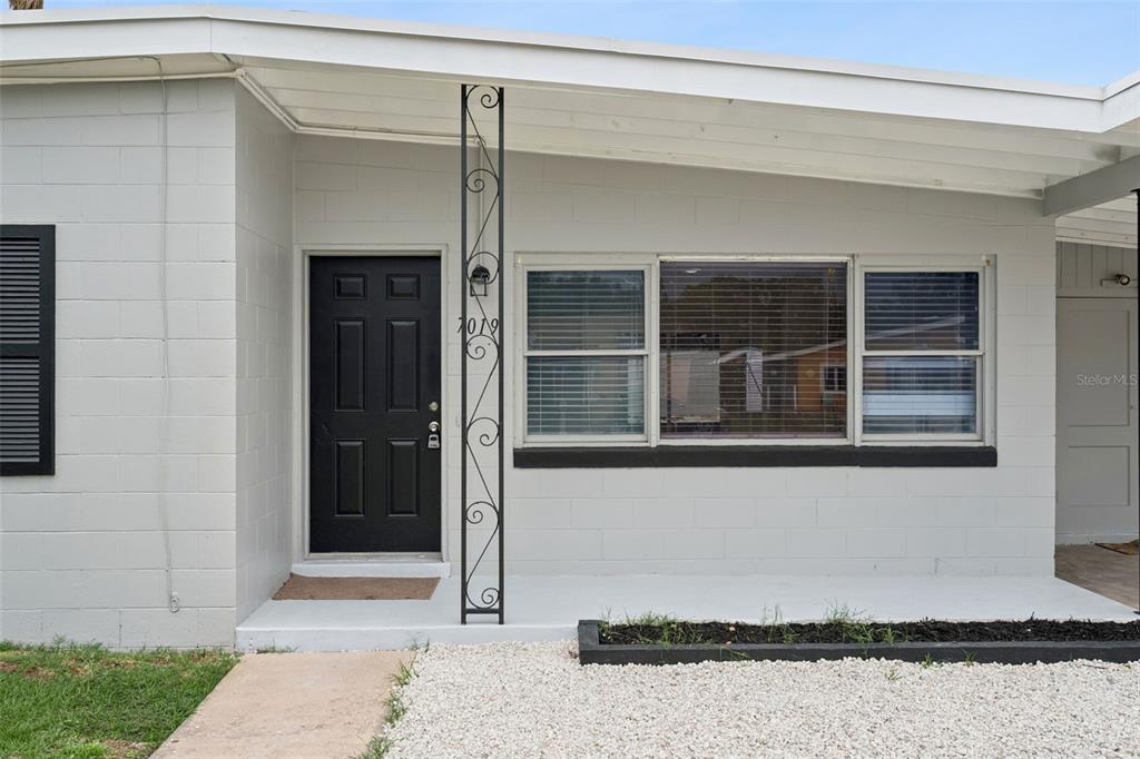 A gray concrete block house exterior features a black front door and a decorative metal post — 7019 ALVINA WAY, ORLANDO, FL