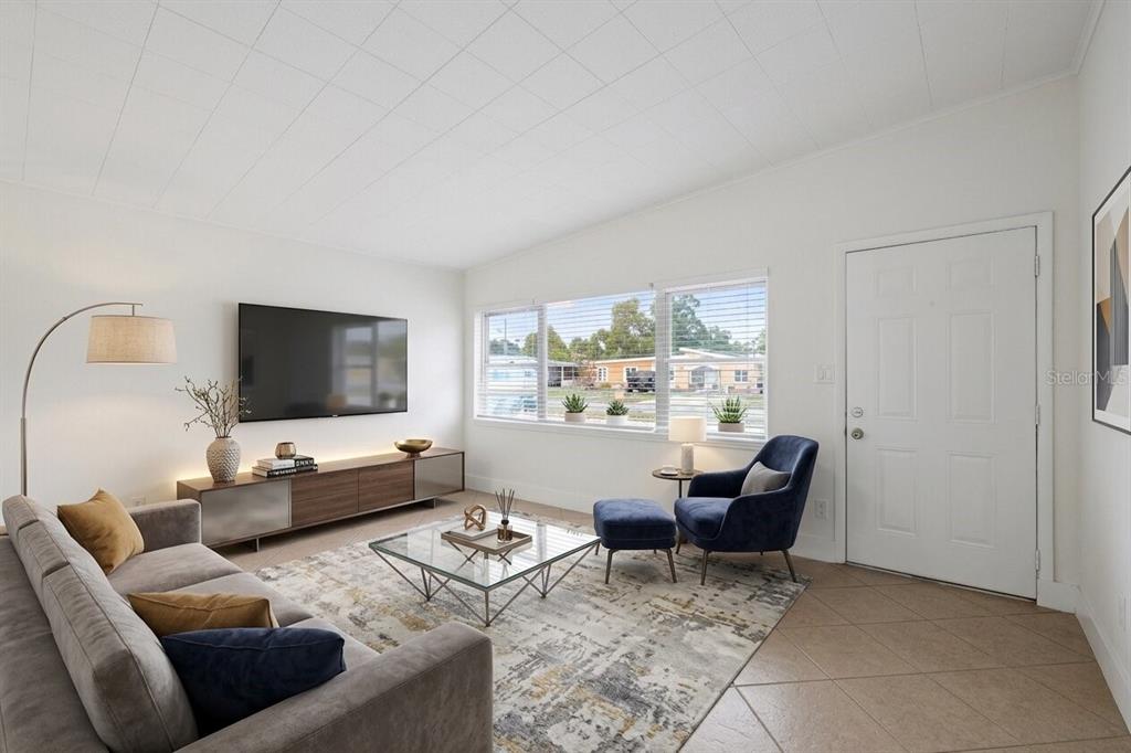 A living room with a gray sofa, blue armchair, glass coffee table, and wall-mounted television — 7019 ALVINA WAY, ORLANDO, FL