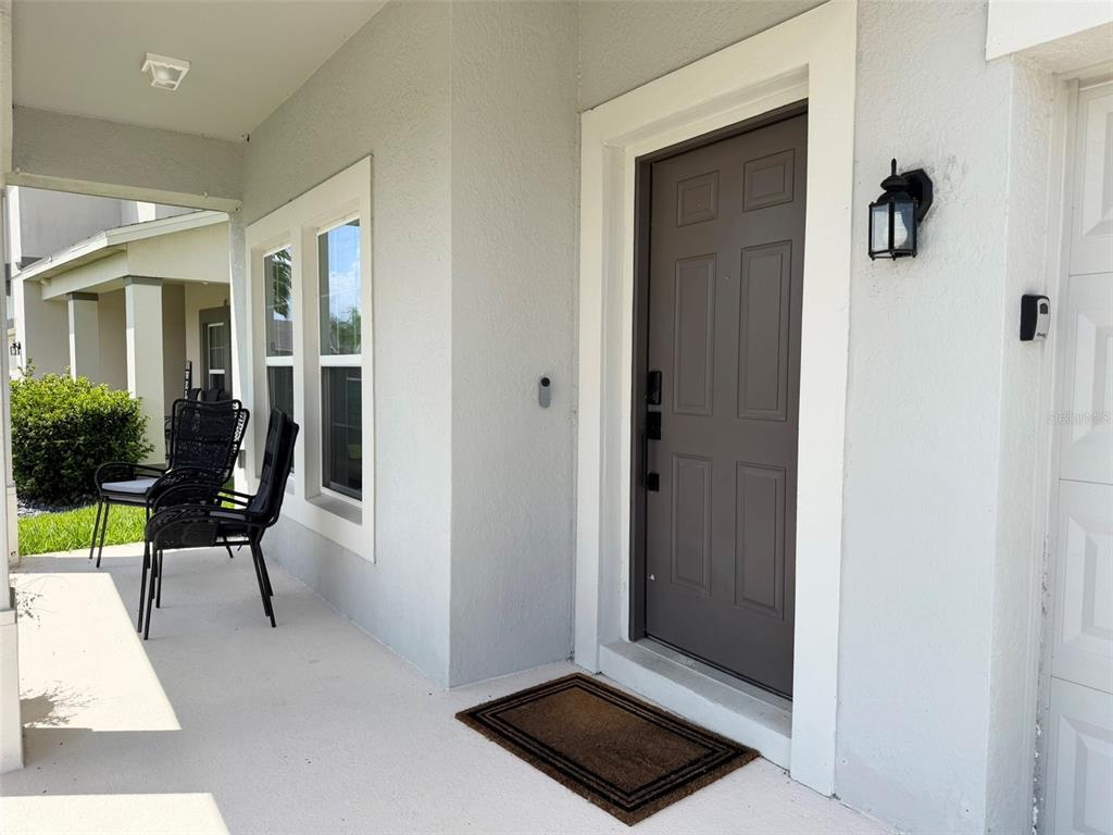 A covered front porch features a brown door, a doormat, and two black chairs — 1659 CHATSWORTH CIRCLE, ST CLOUD, FL