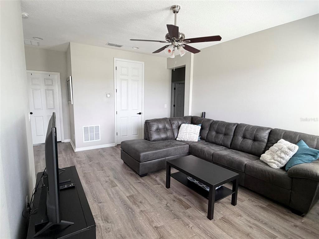 A living room features a grey sectional sofa, a black coffee table, and wood-look flooring — 1659 CHATSWORTH CIRCLE, ST CLOUD, FL
