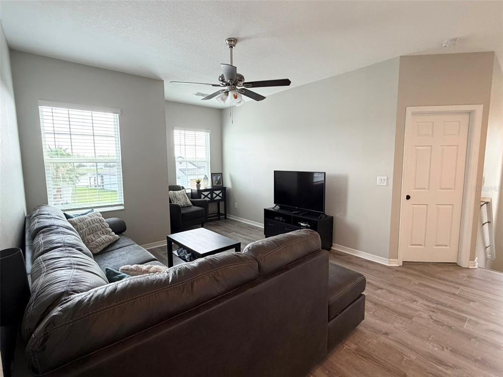 A living room features a dark sectional sofa, a television on a stand, and wood-look flooring — 1659 CHATSWORTH CIRCLE, ST CLOUD, FL