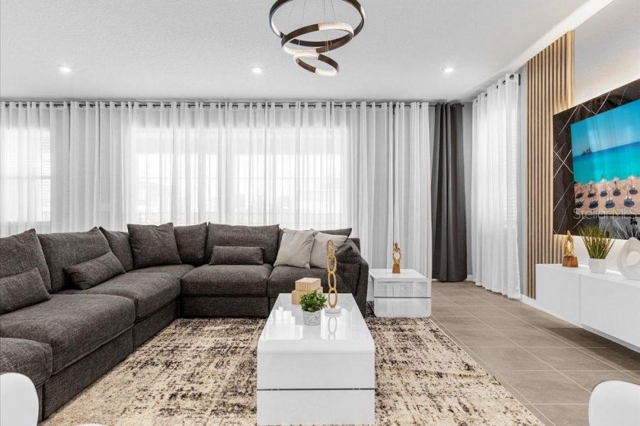 A modern living room features a large gray sectional sofa, a white coffee table, and a television — 9139 TURQUOISE WAVE COVE, KISSIMMEE, FL