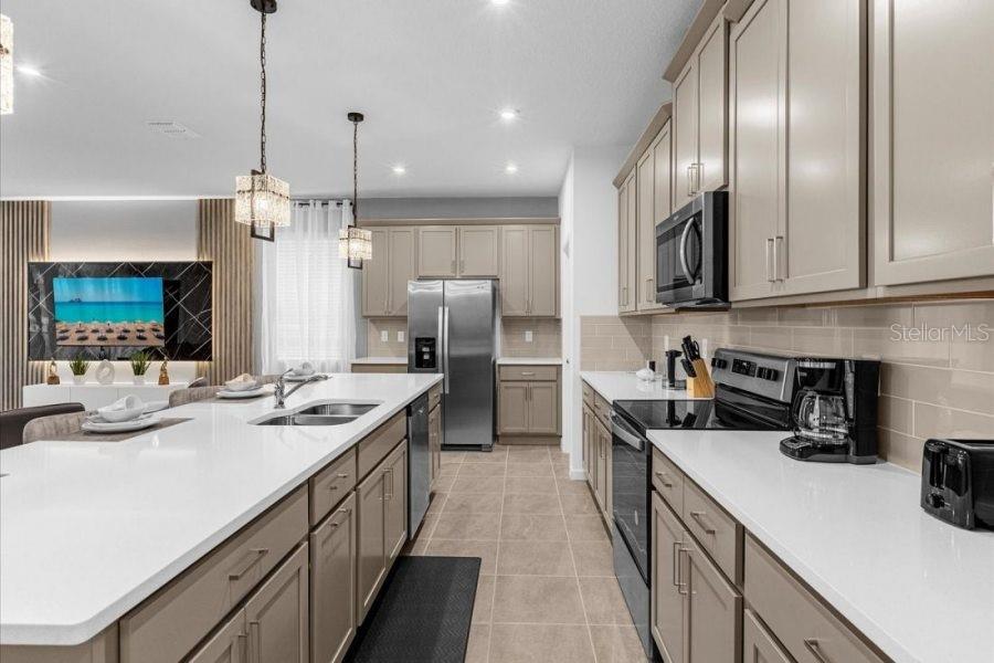 A modern kitchen features light-colored cabinets, white countertops, stainless steel appliances, and a large island — 9139 TURQUOISE WAVE COVE, KISSIMMEE, FL