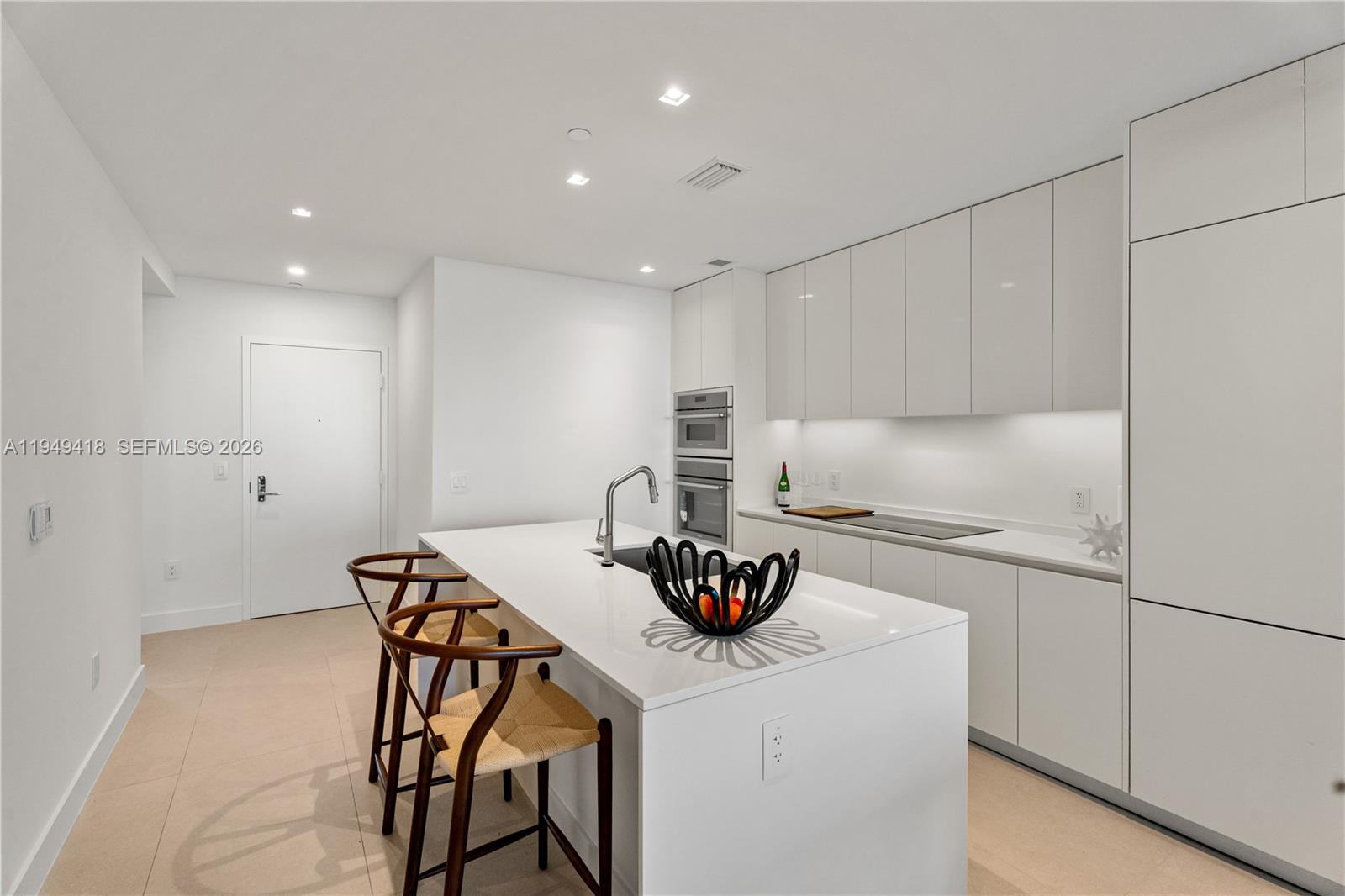 A modern kitchen features white cabinetry, a central island with bar stools, and recessed lighting — 700 NE 24th St # 2602, Miami FL 33137, MIAMI, FL