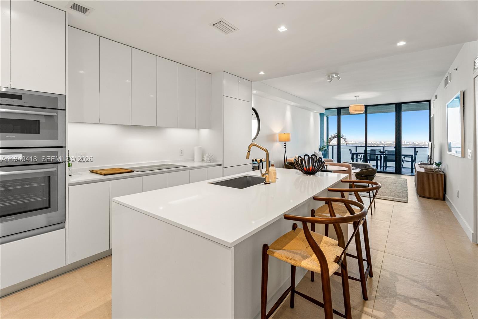 A modern white kitchen features a central island, stainless steel appliances, and a balcony view — 700 NE 24th St # 2602, Miami FL 33137, MIAMI, FL