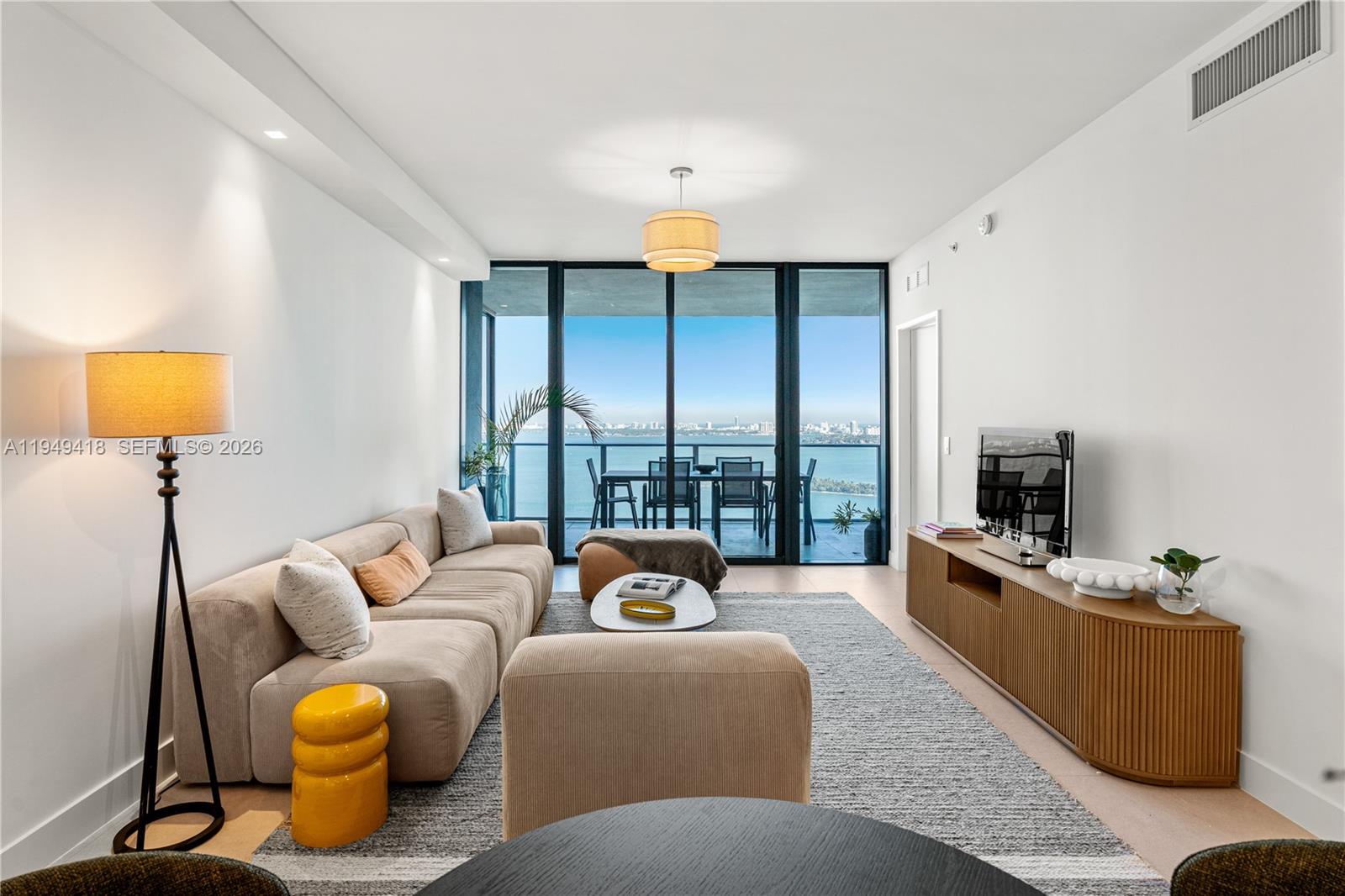 A modern living room features a beige sectional sofa, wood media console, and balcony view — 700 NE 24th St # 2602, Miami FL 33137, MIAMI, FL