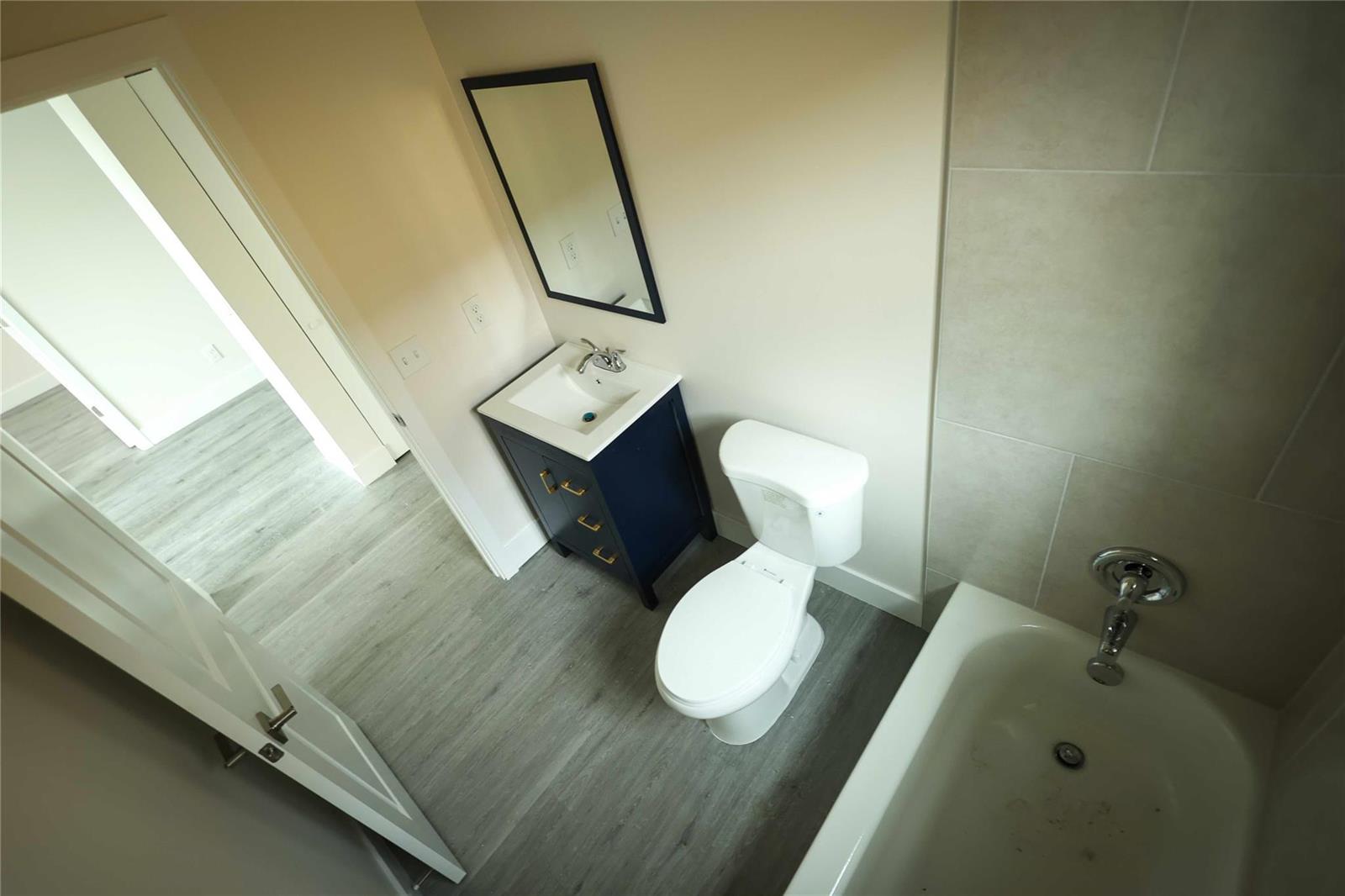 A bathroom featuring a navy vanity, white toilet, and a bathtub with light-colored wall tiles — 732 19th Street, West Palm Beach FL 33407, WEST PALM BEACH, FL