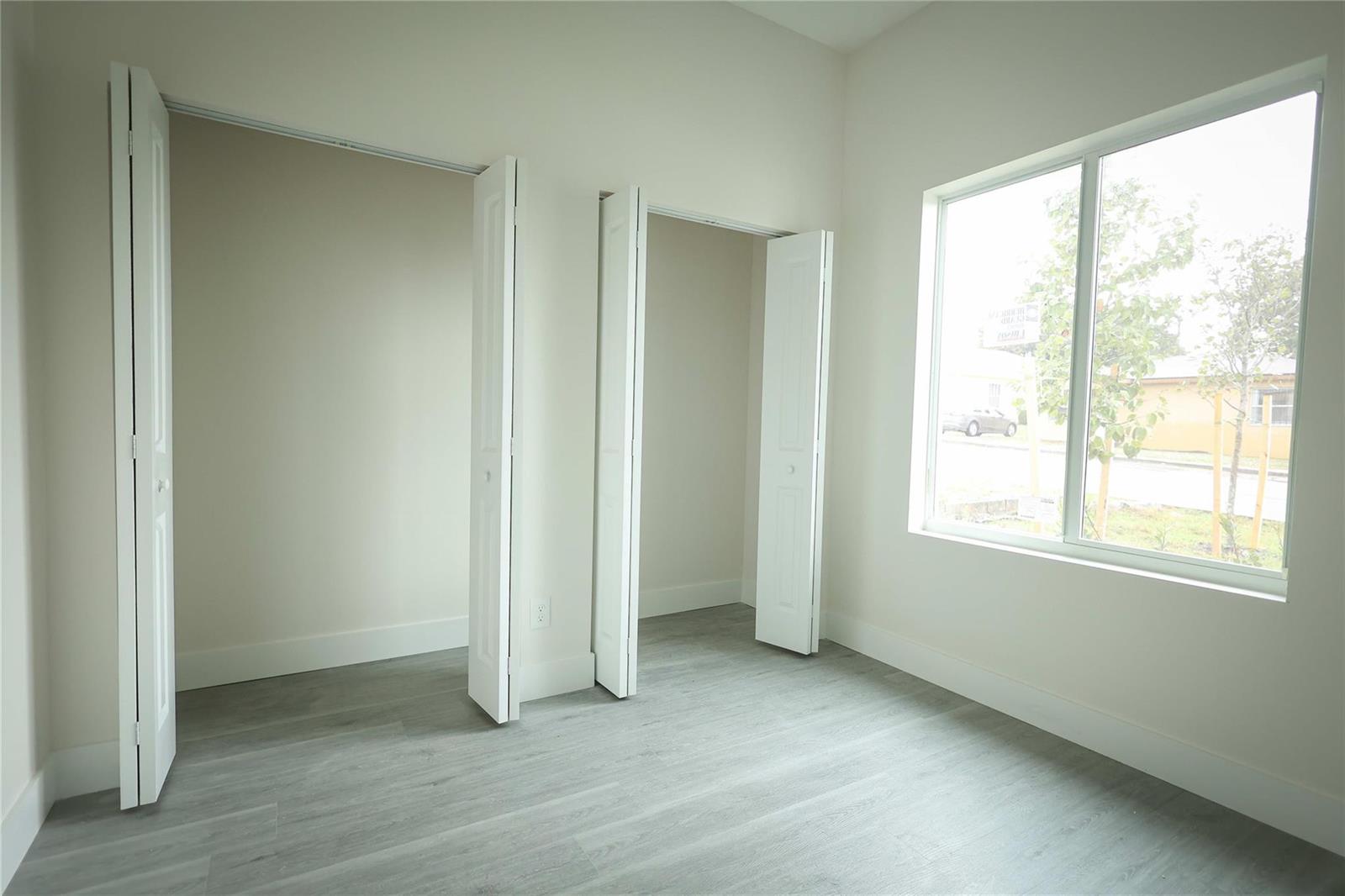 An empty room with light gray flooring, two white bifold closets, and a large window — 732 19th Street, West Palm Beach FL 33407, WEST PALM BEACH, FL