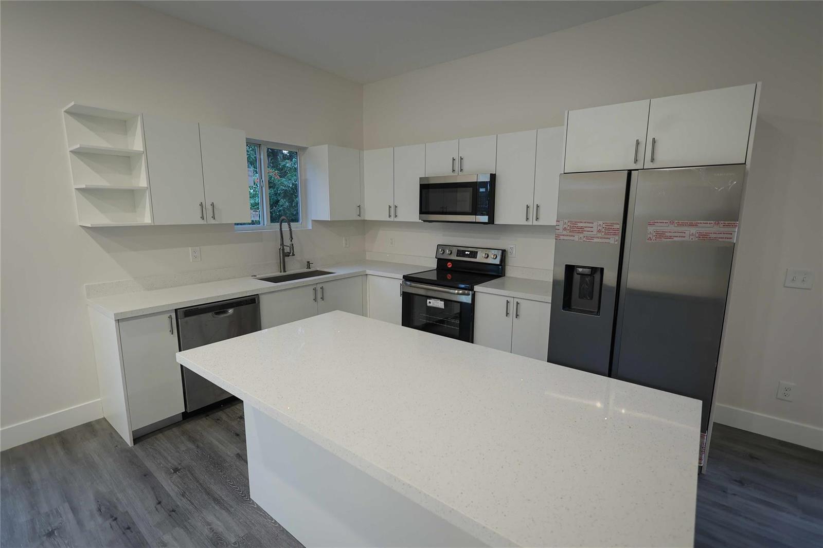 A modern kitchen features white cabinets, stainless steel appliances, a quartz island, and gray flooring — 732 19th Street, West Palm Beach FL 33407, WEST PALM BEACH, FL