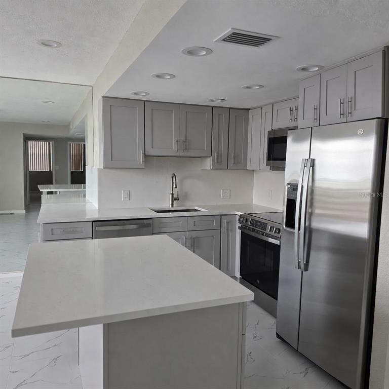 A modern kitchen features gray cabinets, white countertops, stainless steel appliances, and white tiled floors — 4015 BAYSHORE BOULEVARD UNIT 7F, TAMPA, FL