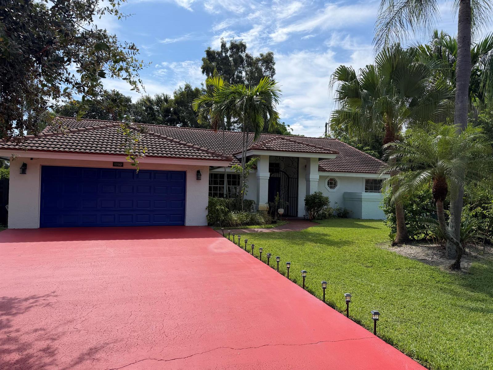 A single-story house with a red driveway, blue garage door, and a tiled roof — 1770 Emilio Lane, Palm Springs FL 33406, PALM SPRINGS, FL