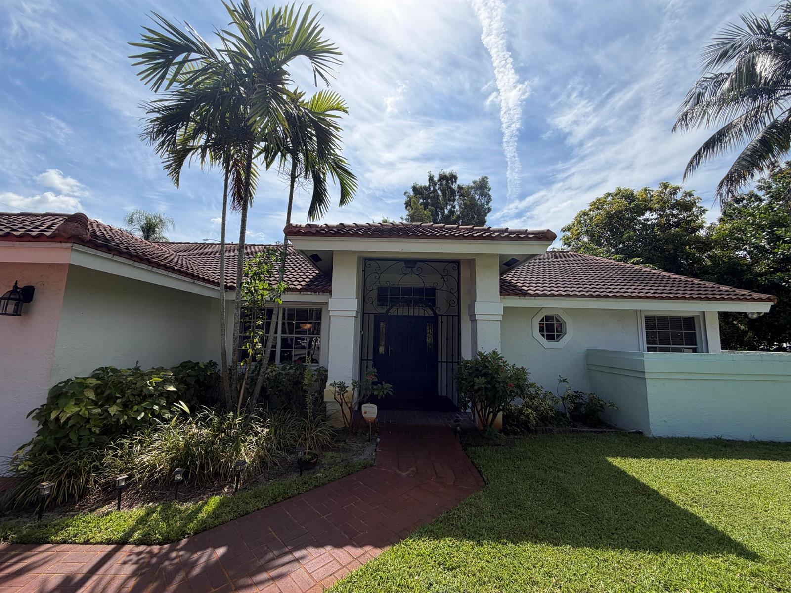A single-story house with a tiled roof, palm trees, and a brick walkway leading to entrance — 1770 Emilio Lane, Palm Springs FL 33406, PALM SPRINGS, FL