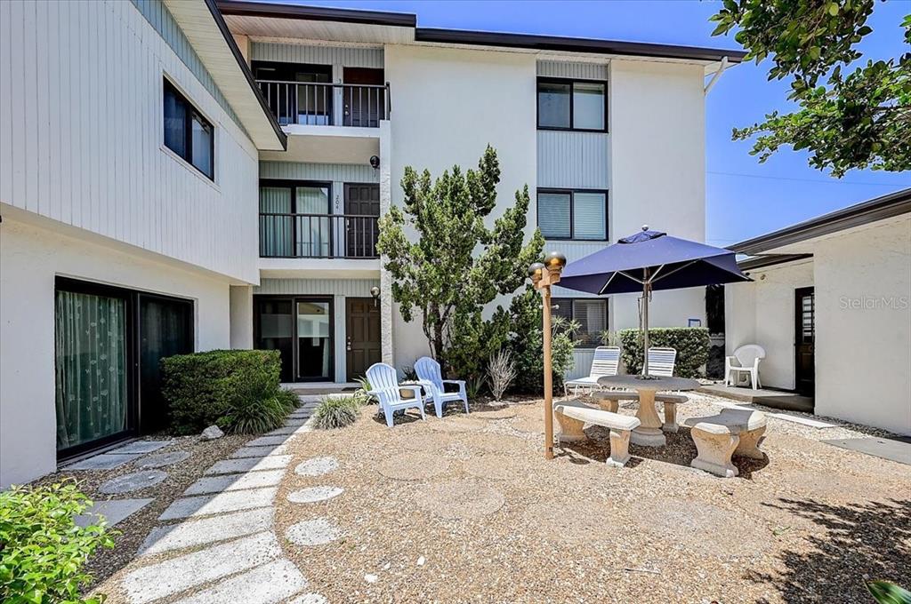 A courtyard with a stone patio, outdoor seating, and a blue umbrella between apartment buildings — 722 S BLVD OF THE PRESIDENTS UNIT 105, SARASOTA, FL