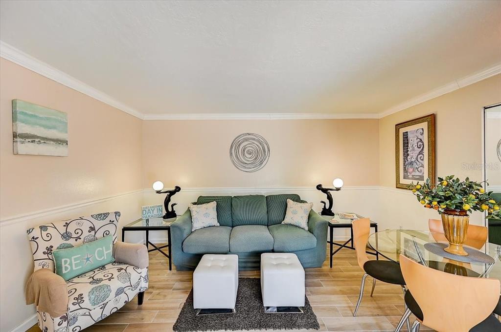 A living room features a green sofa, white ottomans, a patterned armchair, and dining furniture — 722 S BLVD OF THE PRESIDENTS UNIT 105, SARASOTA, FL