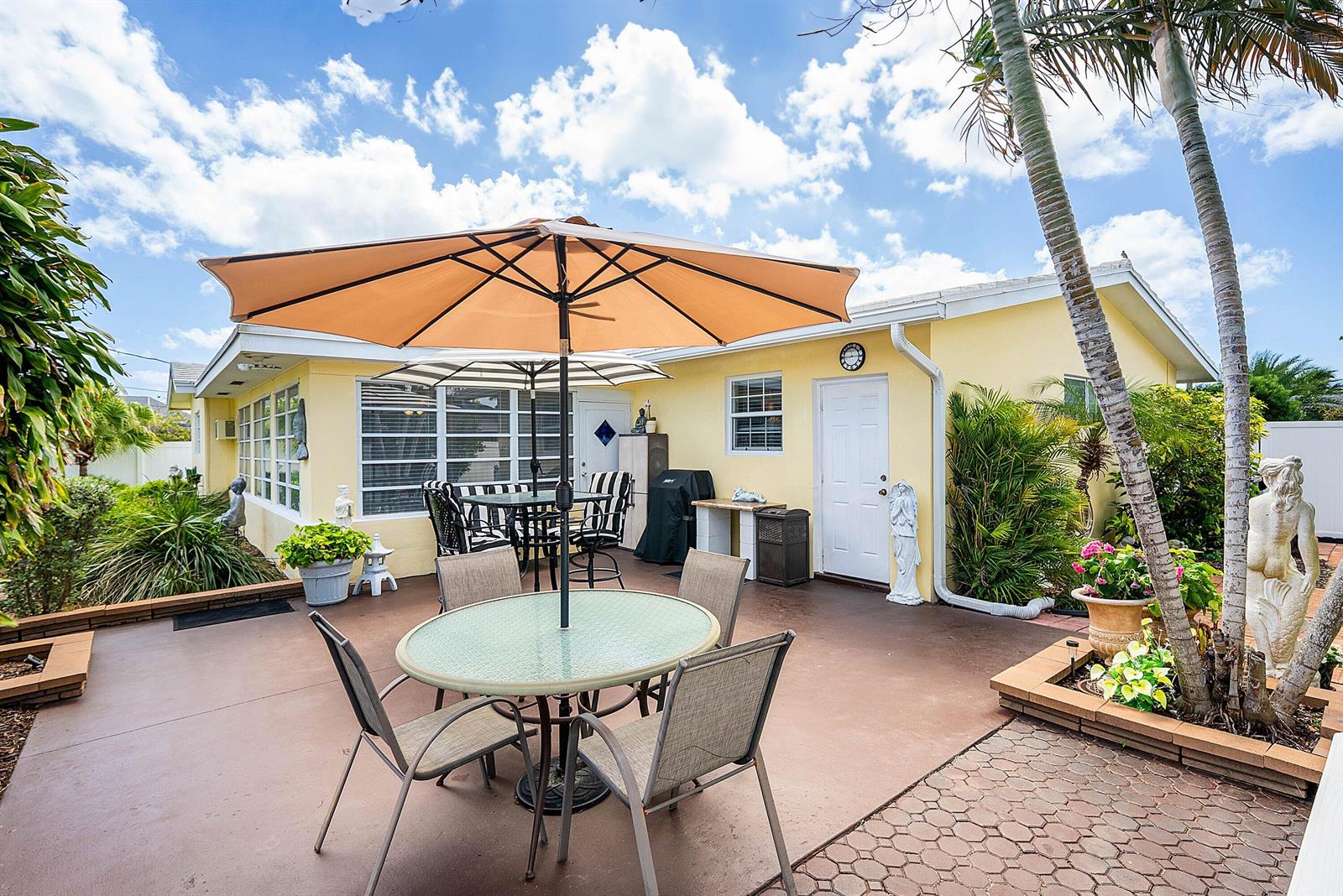 A patio with two dining sets, umbrellas, and a yellow house exterior under a blue sky — 2741 NE 52nd Street, Lighthouse Point FL 33064, LIGHTHOUSE POINT, FL