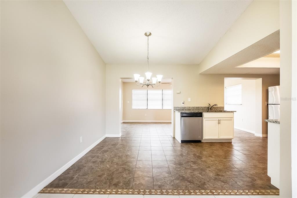 A dining area with tile flooring leads to a kitchen featuring white cabinets and granite countertops — 2072 DUMAS DRIVE, DELTONA, FL
