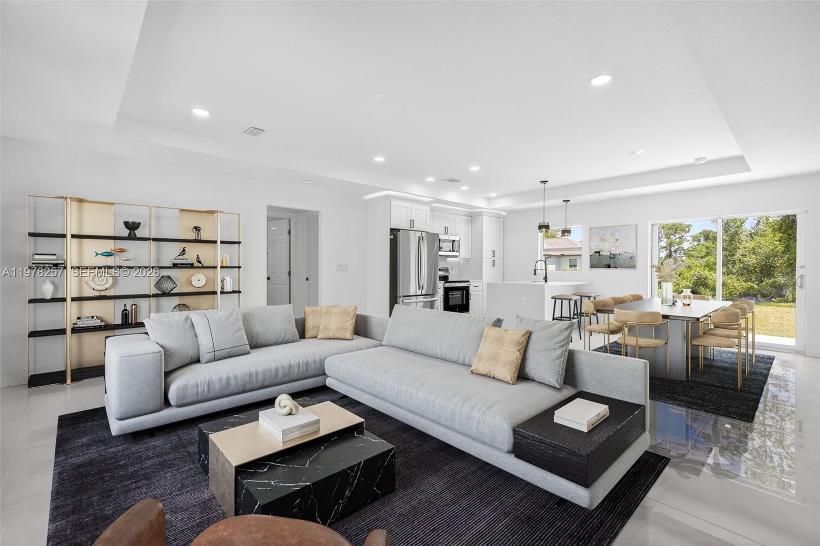 An open-concept living and dining area features a modern kitchen, gray sectional, and marble table — 2916 Dora, Lehigh Acres FL 33974, LEHIGH ACRES, FL