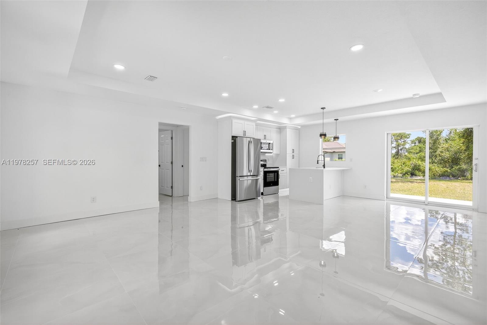 A bright, open-concept kitchen and living area features white cabinetry, stainless appliances, and glossy flooring — 2916 Dora, Lehigh Acres FL 33974, LEHIGH ACRES, FL