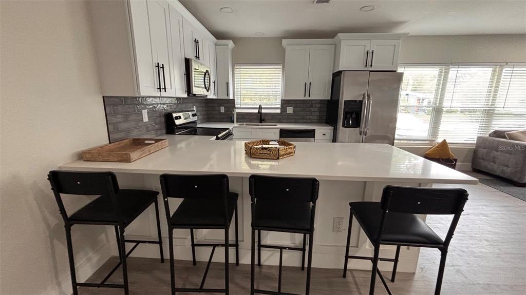 An open-concept kitchen with white cabinets and a breakfast bar overlooks a living room — 2816 HARGILL DRIVE, ORLANDO, FL