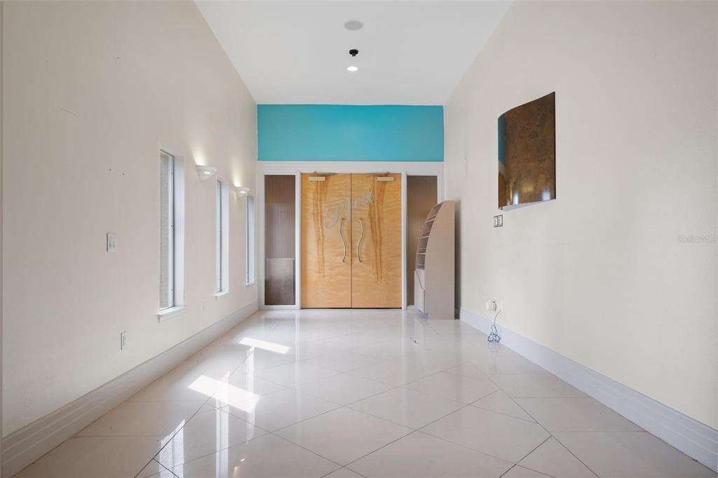 A bright, empty room features light-colored tile floors, tall double doors, and a turquoise accent wall — 3730 TAMPA ROAD UNIT 3730-B, PALM HARBOR, FL