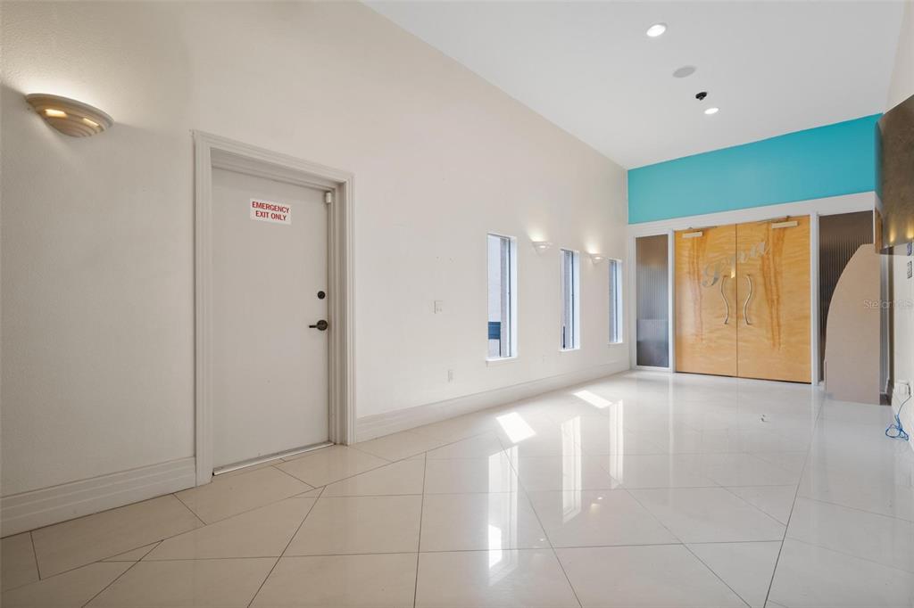 A bright, minimalist room features white tile floors, a white emergency door, and wooden double doors — 3730 TAMPA ROAD UNIT 3730-B, PALM HARBOR, FL