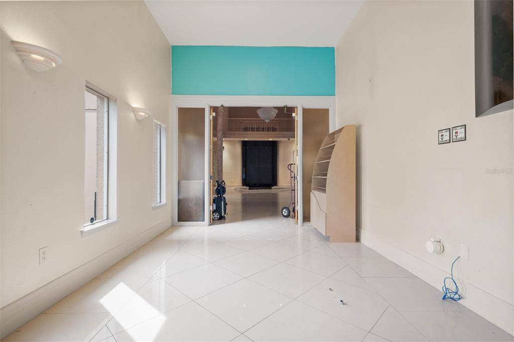 A bright, empty room with white tile floors leads through glass doors to a foyer — 3730 TAMPA ROAD UNIT 3730-B, PALM HARBOR, FL