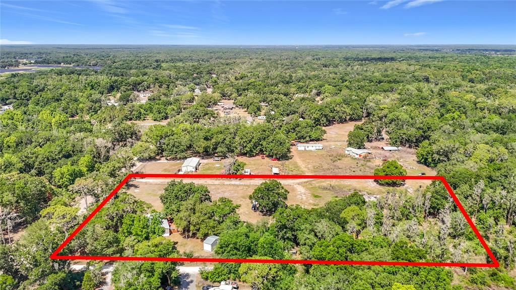 An aerial view shows a large, rectangular plot of land with trees and small structures — 40949 JERRY ROAD, ZEPHYRHILLS, FL