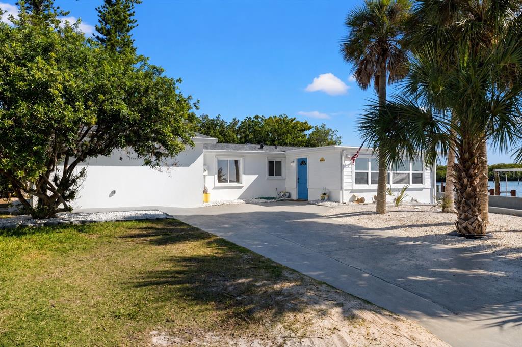 A white single-story house with a blue front door and a concrete driveway near water — 6927 21ST STREET W, BRADENTON, FL