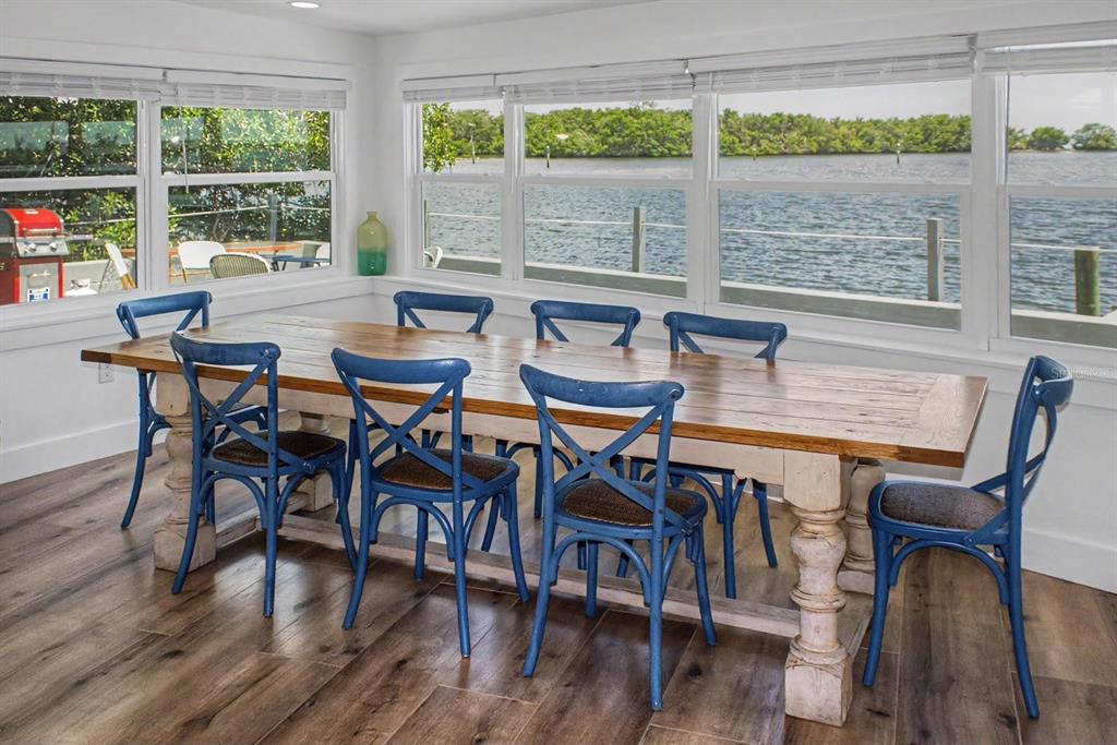 A dining room with a long wooden table, blue cross-back chairs, and large waterfront windows — 6927 21ST STREET W, BRADENTON, FL
