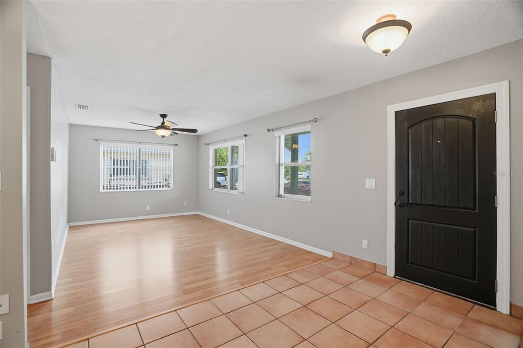 An interior view of a living room featuring light wood flooring, tile entry, and gray walls — 4307 W WISCONSIN COURT, TAMPA, FL