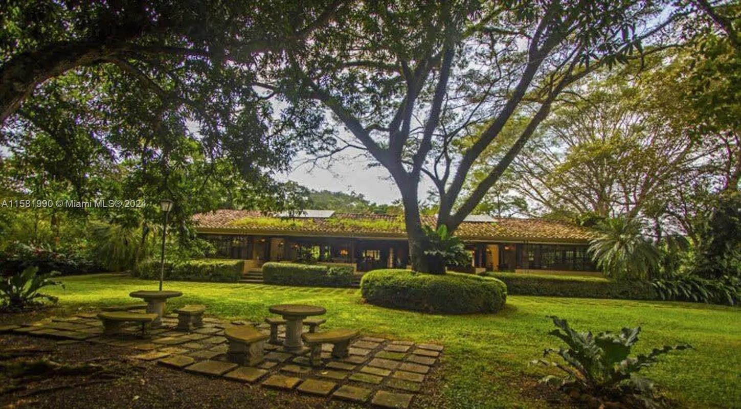A large house with a tiled roof sits behind a lawn featuring stone patio furniture — 9 Santa Rita de OROTINA Casa de Campo Costa Rica., Al, Al